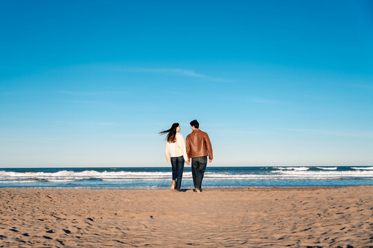 Couple holding hands walking along beach shoreline