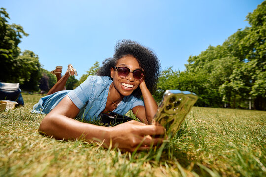 Happy woman relaxes on a lawn, holding her smartphone