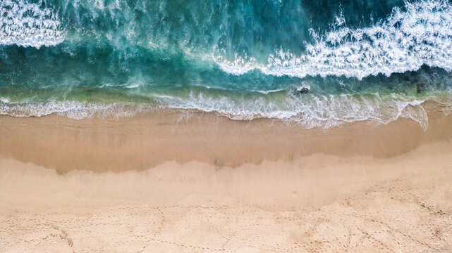 aerial vertical view of turquoise waves meeting sandy beach