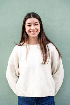 Young woman smiling, standing against green wall