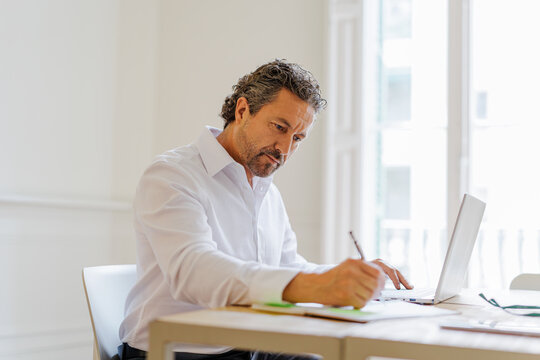 Professional taking notes and typing on laptop at office