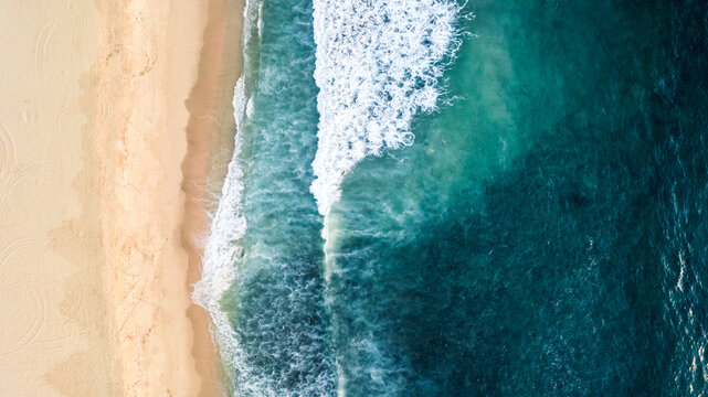 aerial overhead view of turquoise waves breaking on sandy beach