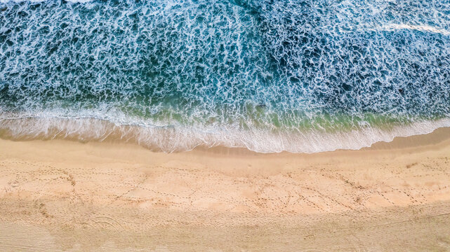 aerial view of blue ocean waves breaking on wide sandy beach