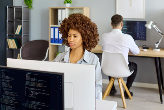 Woman developer programmer coding at computer in office. She works on software at a desktop monitor, reviewing code and enhancing app quality in a bright workspace. Core tech work concept now.