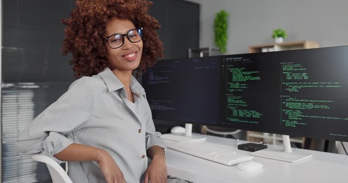 Programmer developer woman coding at computer workstation. Dual screens show code in a tidy office, highlighting focus, agility and technology. Concept of modern software development teamwork.