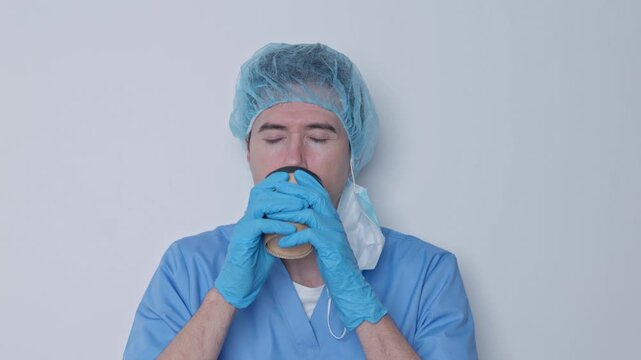 Tired male doctor drinking coffee during break on white background