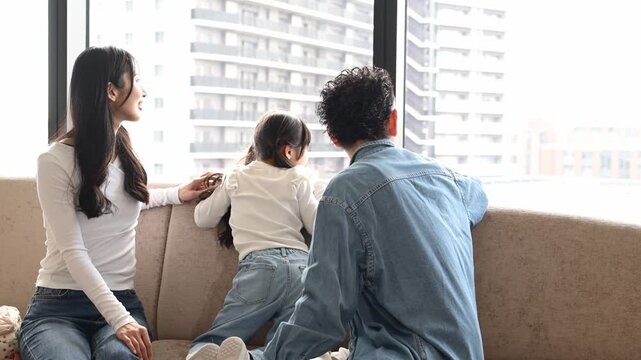 旅行先のホテルで窓の外の景色を眺める30代の日本人夫婦と6歳の子どもの後ろ姿
