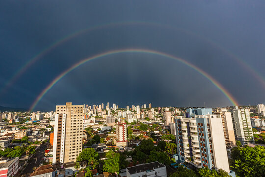 Vista panor&acirc;mica de arco-&iacute;ris duplo sobre os edif&iacute;cios e pr&eacute;dios de uma grande cidade sob c&eacute;u de tempestade