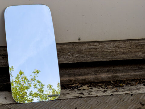 mirror reflecting the clear blue sky above , resting against a dirty abandoned building 