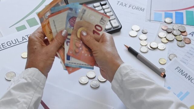 Person counting euro cash, coins with Tax forms, accounting documents, graphics, calculator, a blank planning sheet placed on an office desk. Planning, accounting of expenses and income for a business