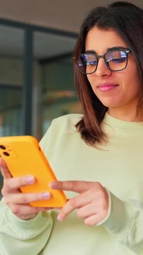 Young it specialist business woman manager using cell phone mobile application for online work. Latin Hispanic female girl student or freelance worker holding smartphone standing in office. Vertical