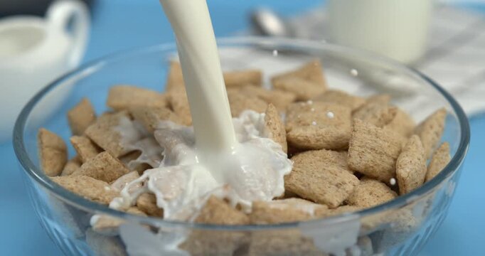 Milk pouring into wheat cereal pillows in bowl with splash in super slow motion