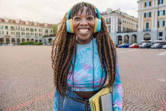 Smiling student with headphones holding laptop in city
