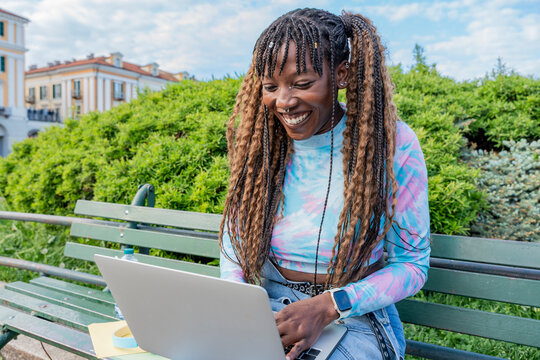 Smiling woman using laptop on park bench outdoors