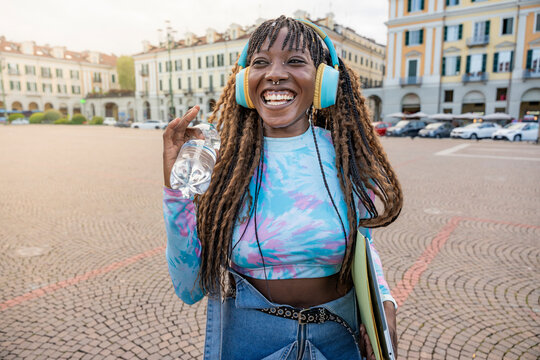 Smiling woman with headphones holding water in city square