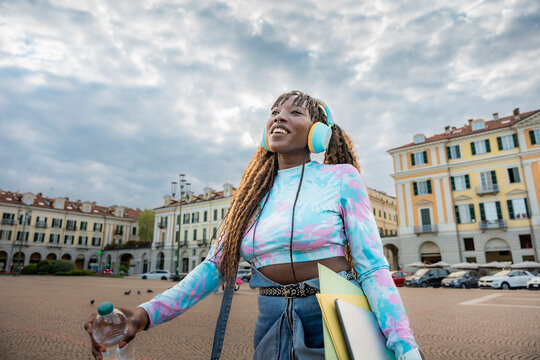 Smiling woman with headphones walking in city square