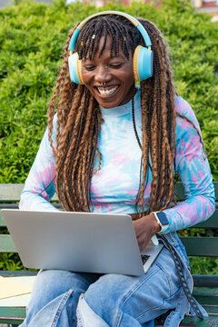 Smiling woman with headphones using laptop on park bench