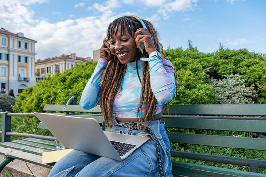 Smiling student using laptop and headphones on park bench