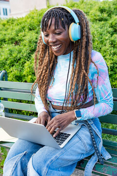 Young woman with headphones using laptop on park bench