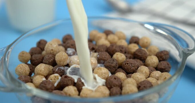 Milk pouring into wheat cereal corn balls in bowl with splash in super slow motion