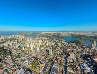 Fototapeta premium Aerial panoramic view of Vitória, Espírito Santo, Brazil, featuring Vitória Bay, islands, mountains, urban skyline, coastline, and clear blue sky captured by drone.