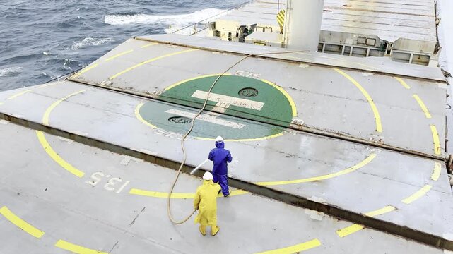 crew members washing hatch covers of ship cargo holds by sea water. vessel undeway. hand work of seafarers at sea.