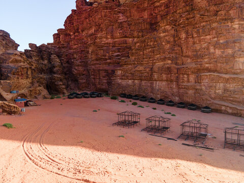 Aerial view of Wadi Rum Protected Area featuring traditional Bedouin tents nestled against towering red sandstone cliffs in the desert landscape of Aqaba Governorate, Jordan.