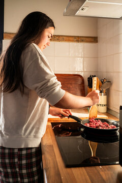 Girl cooks minced meat in a cozy home kitchen on stove