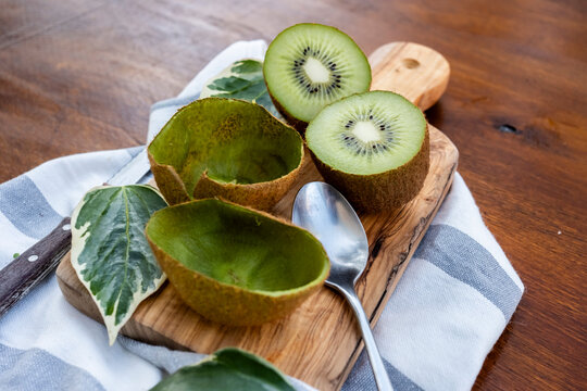 Fresh kiwi fruit halves on wooden board with spoon and knife