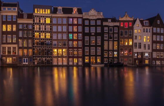Dancing houses along Amsterdam canal at night with reflections