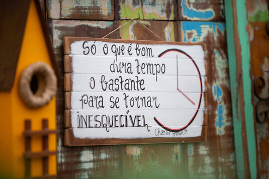 Placa decorativa de madeira com frase motivacional manuscrita pendurada em parede r&uacute;stica ao lado de casinha de passarinho