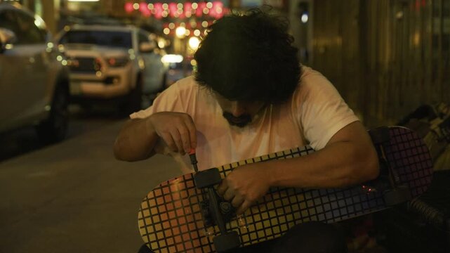 Man Using Screwdriver on Skateboard Truck At Night On San Francisco Chinatown Street