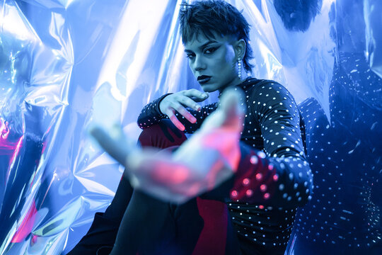 Cyberpunk young woman in neon-lit studio with foil backdrop