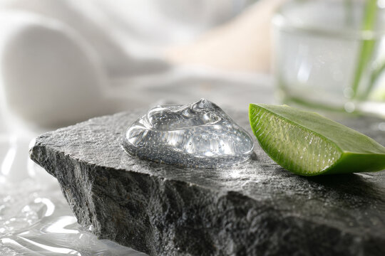 Aesthetic micro shot of a transparent hydrating gel dollop on a broken edge of a dark gray granite block next to a fresh organic aloe vera slice