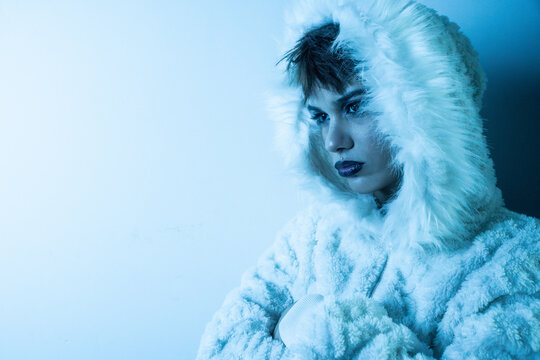 Young woman fashion model in furry hooded coat, blue light