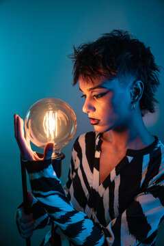 Young fashion model with glowing bulb in moody studio light