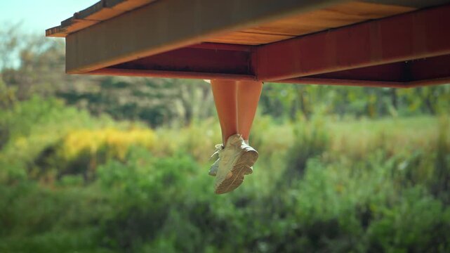 Low angle view of Asian woman wearing sneakers and dangling her legs while sitting on wooden terrace outdoors, young female traveler relaxing in nature garden for weekend getaway, mindfulness.