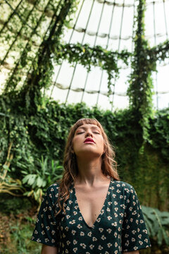 Woman breathing deeply in lush greenhouse surrounded by ivy