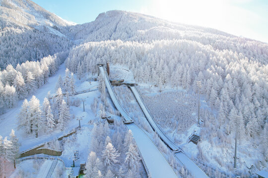 Aerial view of Stadio Olimpico del Salto surrounded by snow-covered pine forests and mountain slopes in Pragelato, Piedmont, Italy.