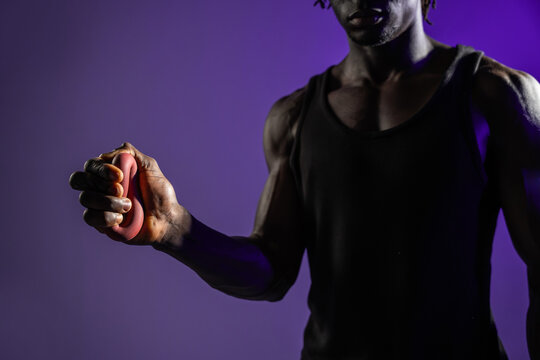 Black athlete squeezing hand gripper in purple studio light