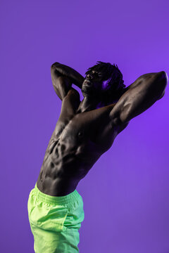 Muscular black athlete posing in purple studio light