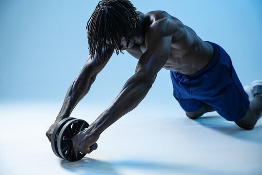 Black athlete using ab wheel for core training in studio