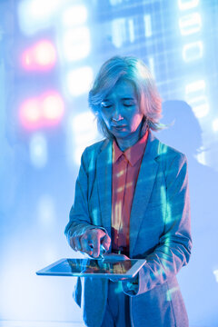 Futuristic senior Asian woman using tablet in neon light