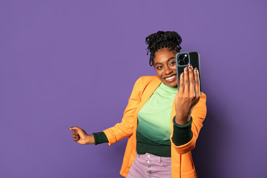 Young afro woman taking selfie in studio on purple wall