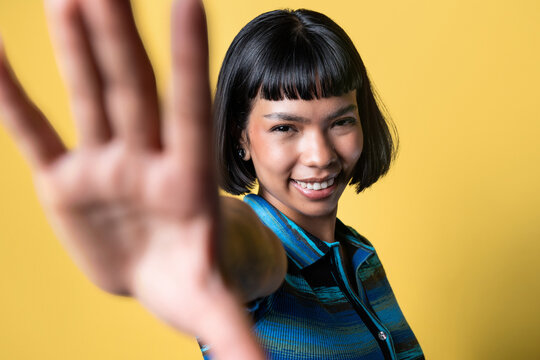 Smiling Latin young woman with stop gesture on yellow