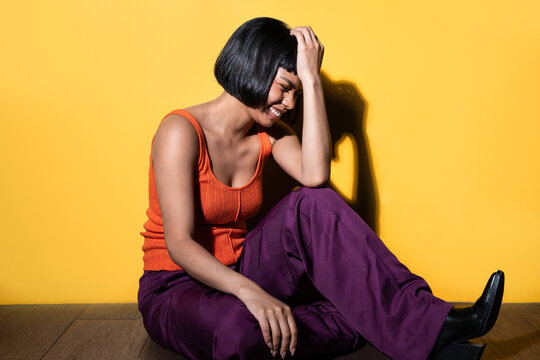 Latin young woman sitting and smiling against yellow wall
