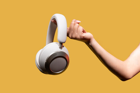 Woman hand holding wireless headphones on yellow studio background
