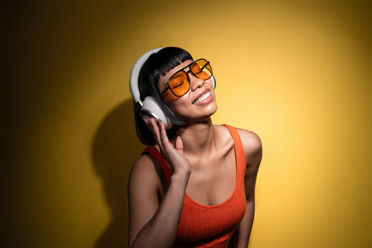 Latin young woman enjoying music with headphones on yellow