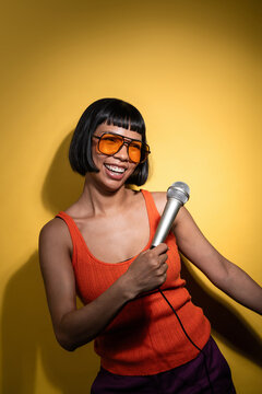 Smiling latin young woman holding microphone on yellow wall
