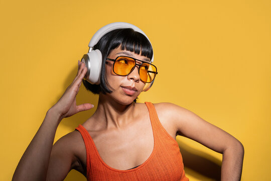 Latin young woman with headphones and sunglasses on yellow